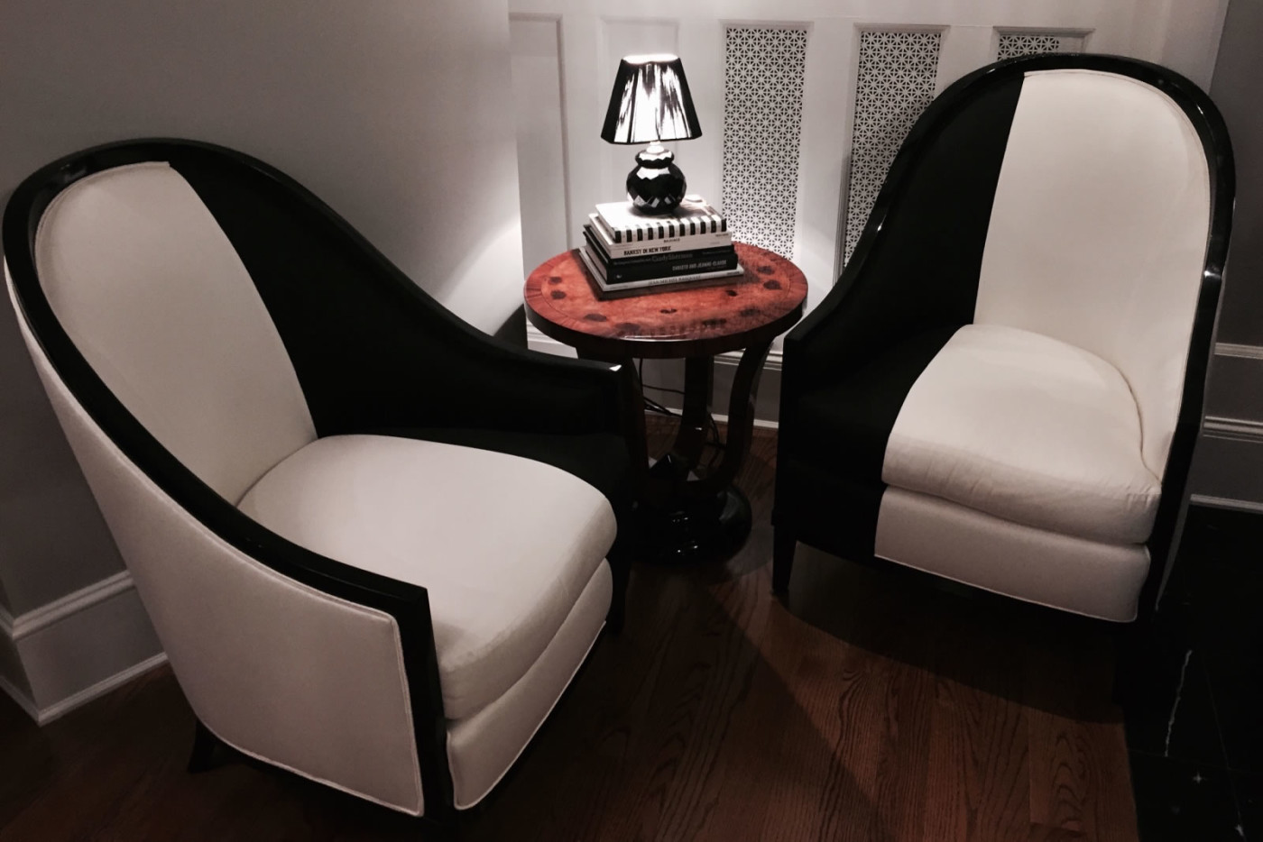 Two black and white modern upholstered chairs for Hillary Clinton with small round wood end table topped with lamp perched on black and white covered books.