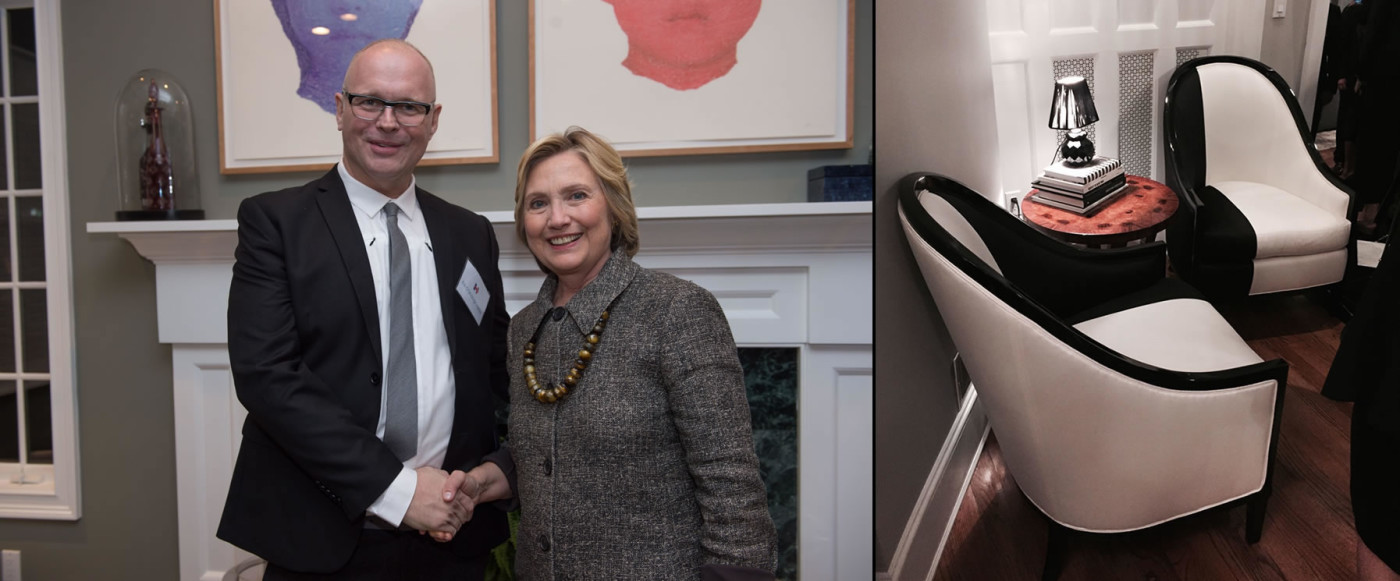 Man shaking hands with gray suit wearing Hillary Clinton in front of white fire place and Additional angle of black and white modern upholstered chairs for Hillary Clinton with small round wood end table topped with lamp perched on black and white covered books.